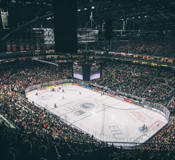 Eine weite Sicht auf ein voll besetztes Eishockeystadion mit Spielern auf dem Eis und einer großen Anzeigetafel.