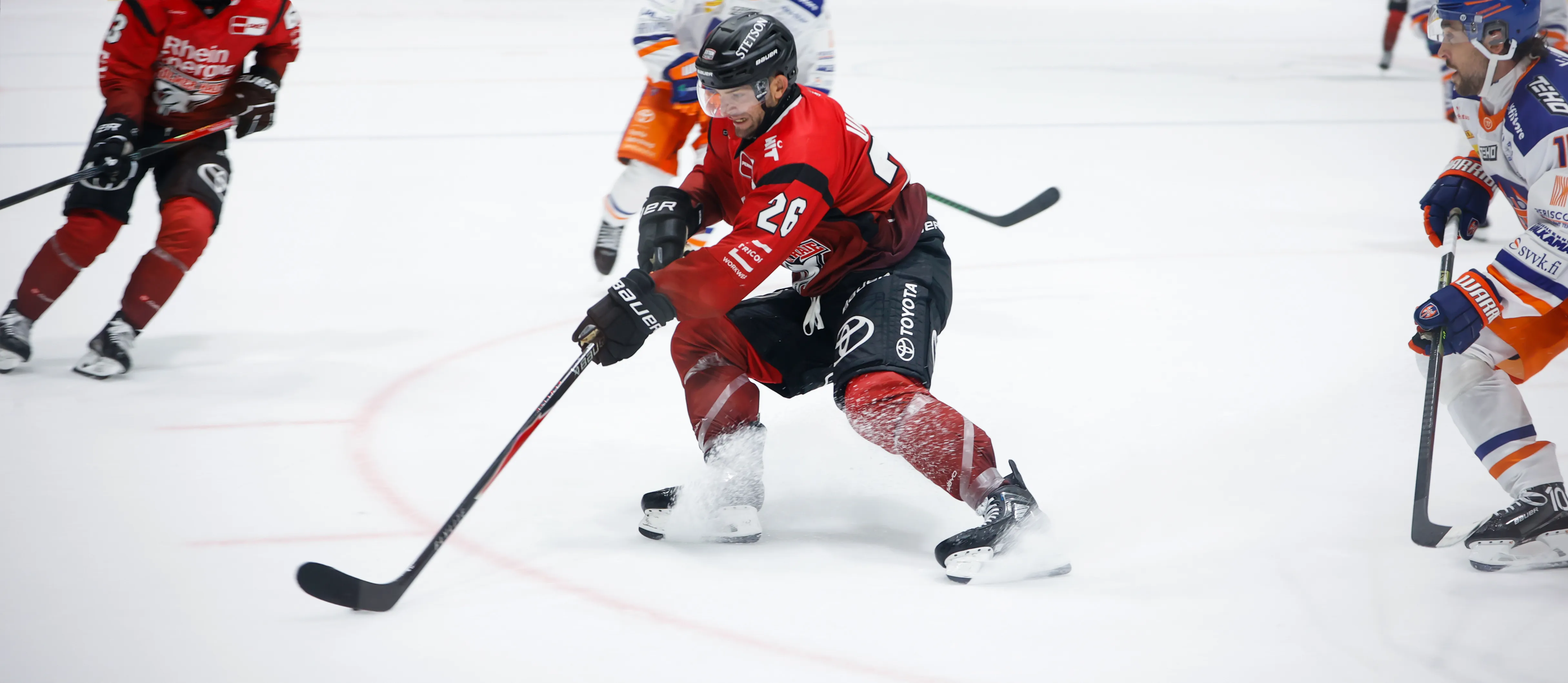 Ein Eishockeyspieler in roter Sportkleidung dribbelt den Puck auf dem Eis.
