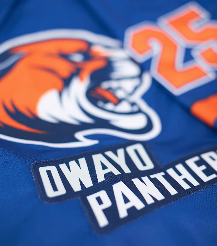 Nahaufnahme eines blauen Sporttrikots mit einem orangefarbenen Panther-Logo und der Aufschrift 'OWAYO PANTHERS' in weißer Schrift auf einem dunklen Aufnäher.