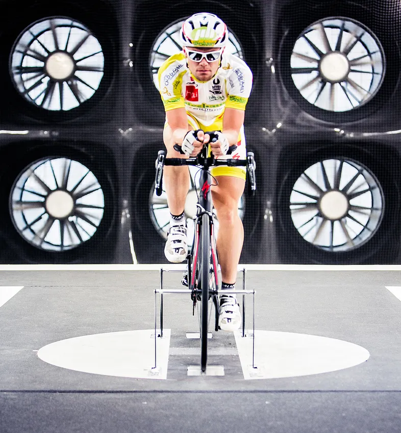 Ein Radfahrer in einer aerodynamischen Position auf einem Fahrradtrainer in einem Windkanal, um die Leistung von maßgeschneiderten Sportbekleidungen zu testen.