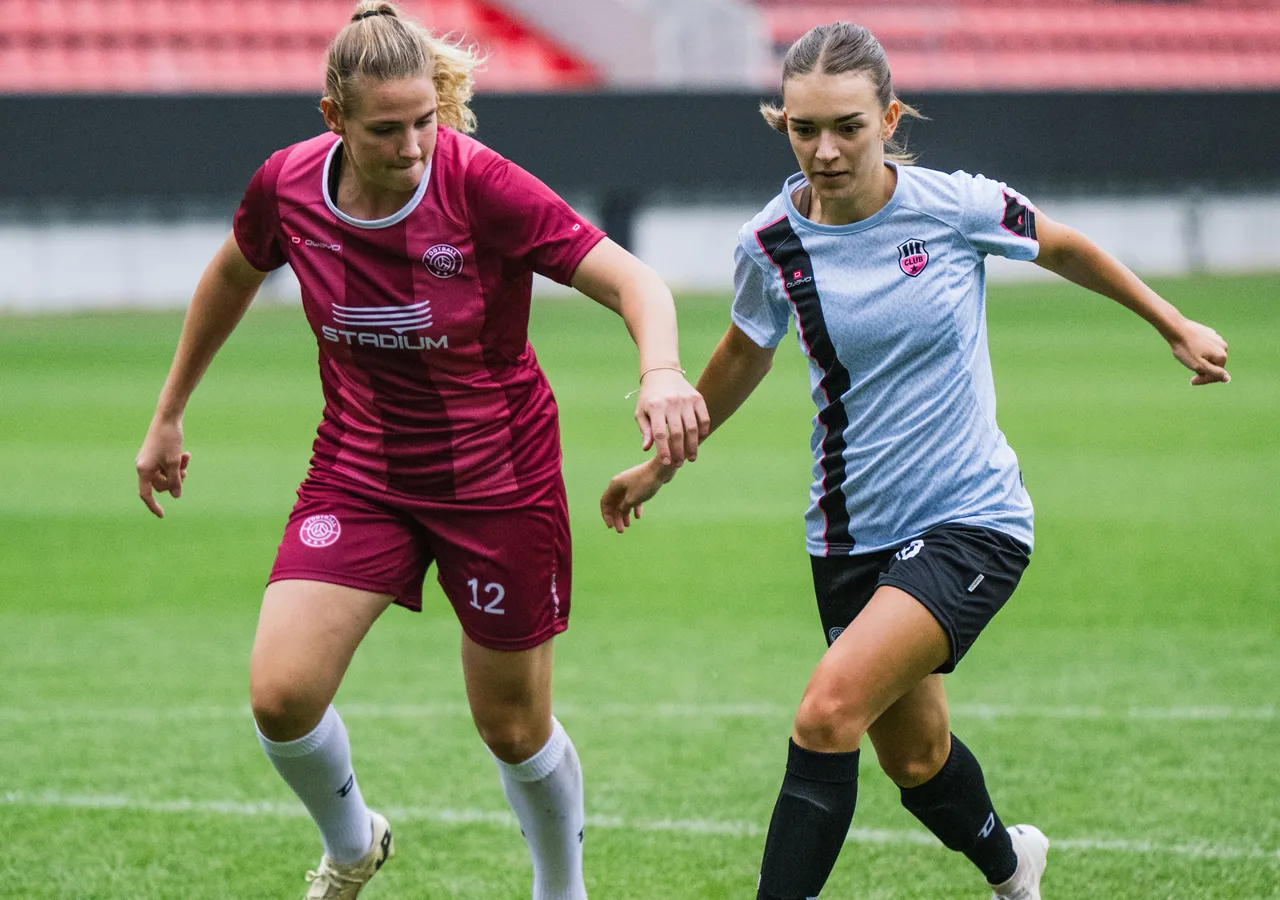 Zwei Frauen in Sportbekleidung spielen Fußball auf einem Rasenplatz.