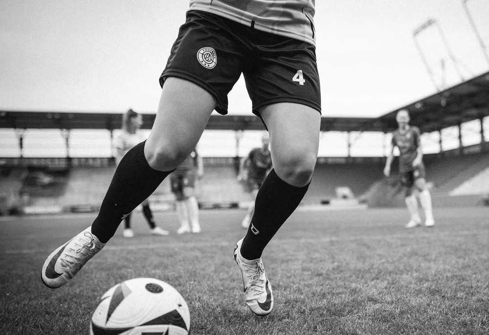 Eine Spielerin in kurzen Fußballhosen und langen Socken dribbelt einen Ball auf dem Spielfeld.