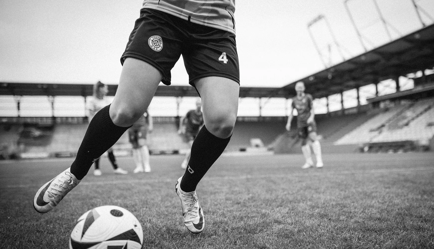 Eine Spielerin in kurzen Fußballhosen und langen Socken tritt den Ball auf einem Fußballplatz.