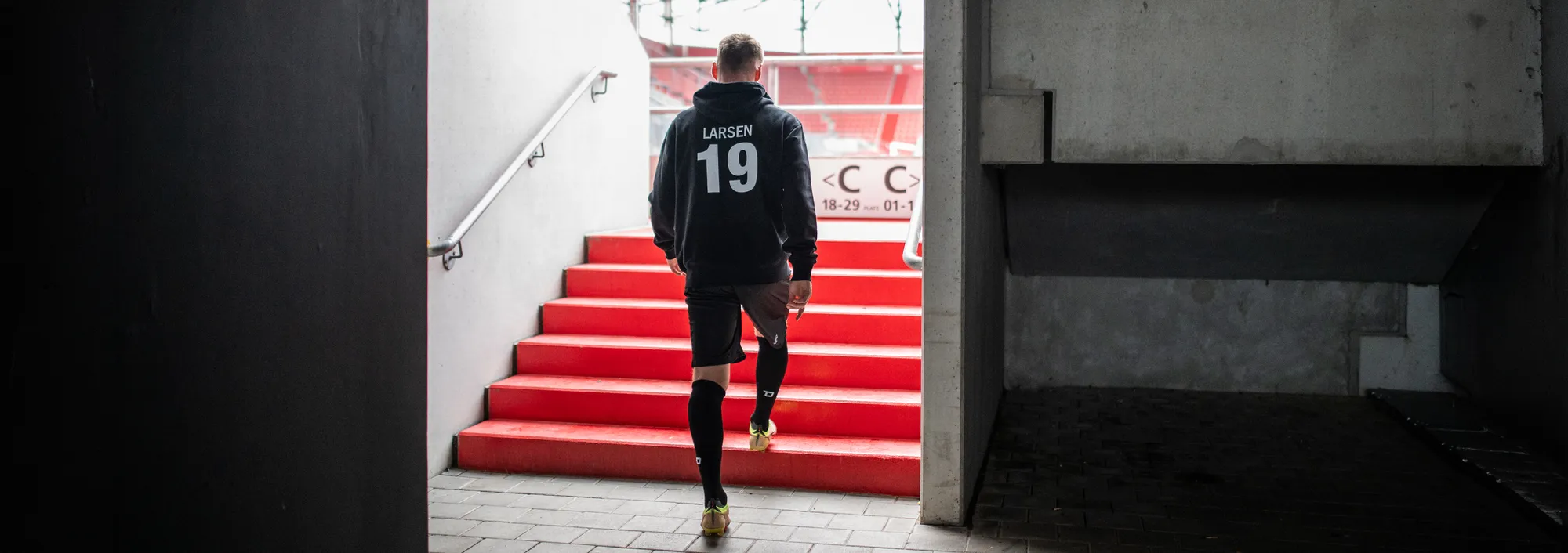 Ein Spieler in einem schwarzen Hoodie mit der Nummer 19 geht die roten Treppen aus einem Stadion hinunter.