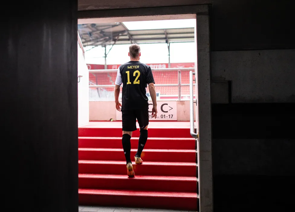 Ein Fußballspieler in einem schwarz-gelben Trikot mit der Nummer 12 geht eine Treppe hinauf.