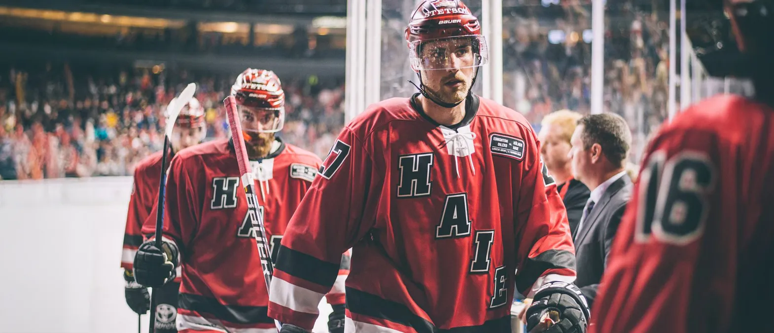 Eishockeyspieler in roten Trikots mit den Buchstaben 'H', 'A', 'I', 'E' und der Nummer 7 auf dem Rücken, die auf dem Eis stehen.