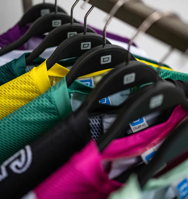 Mehrere farbenfrohe, maßgeschneiderte Sportbekleidungsstücke hängen an schwarzen Bügeln.