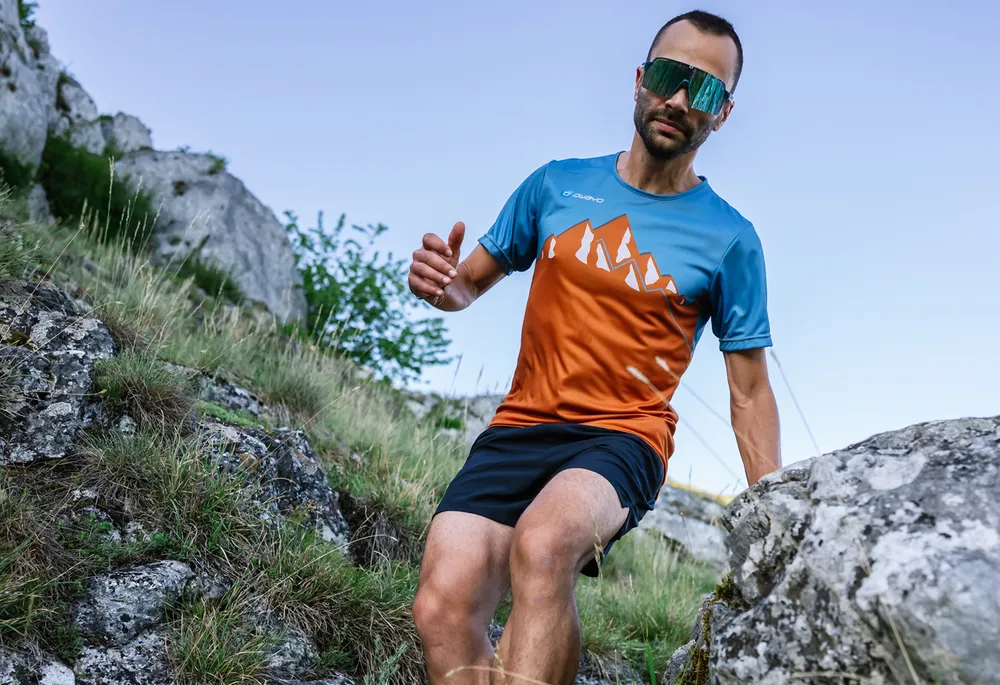 Ein Mann läuft über einen steinigen Pfad in einem bunten Sporttrikot mit Bergdesign.