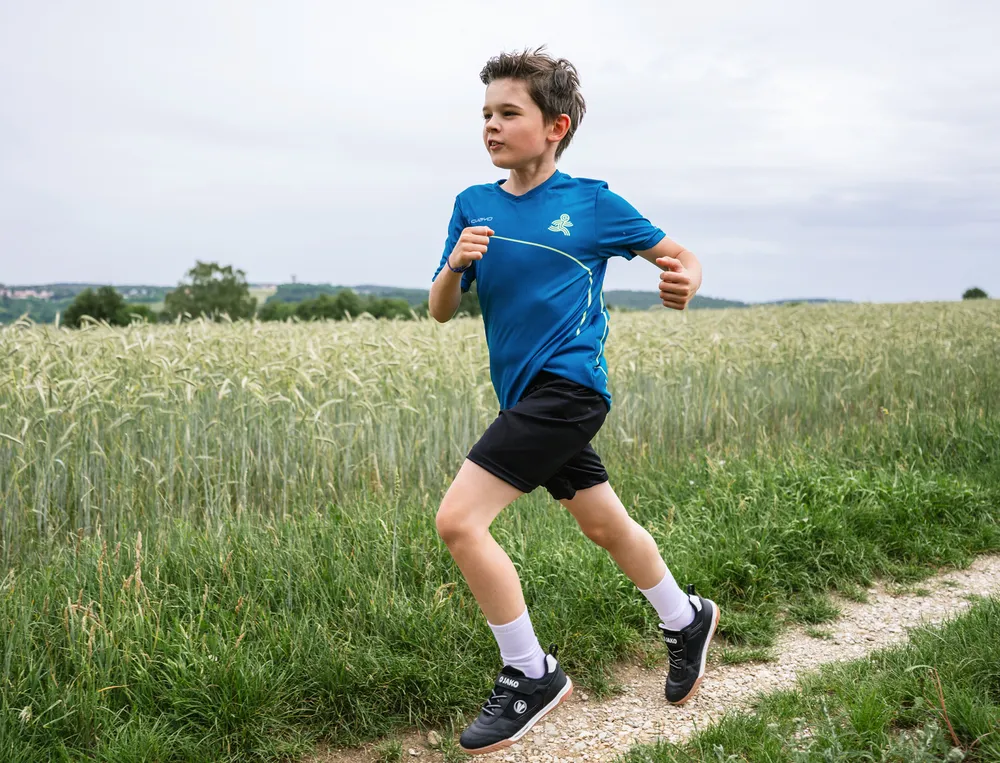 Ein Junge läuft auf einem Feldweg, trägt ein blaues Sporttrikot und kurze schwarze Shorts.
