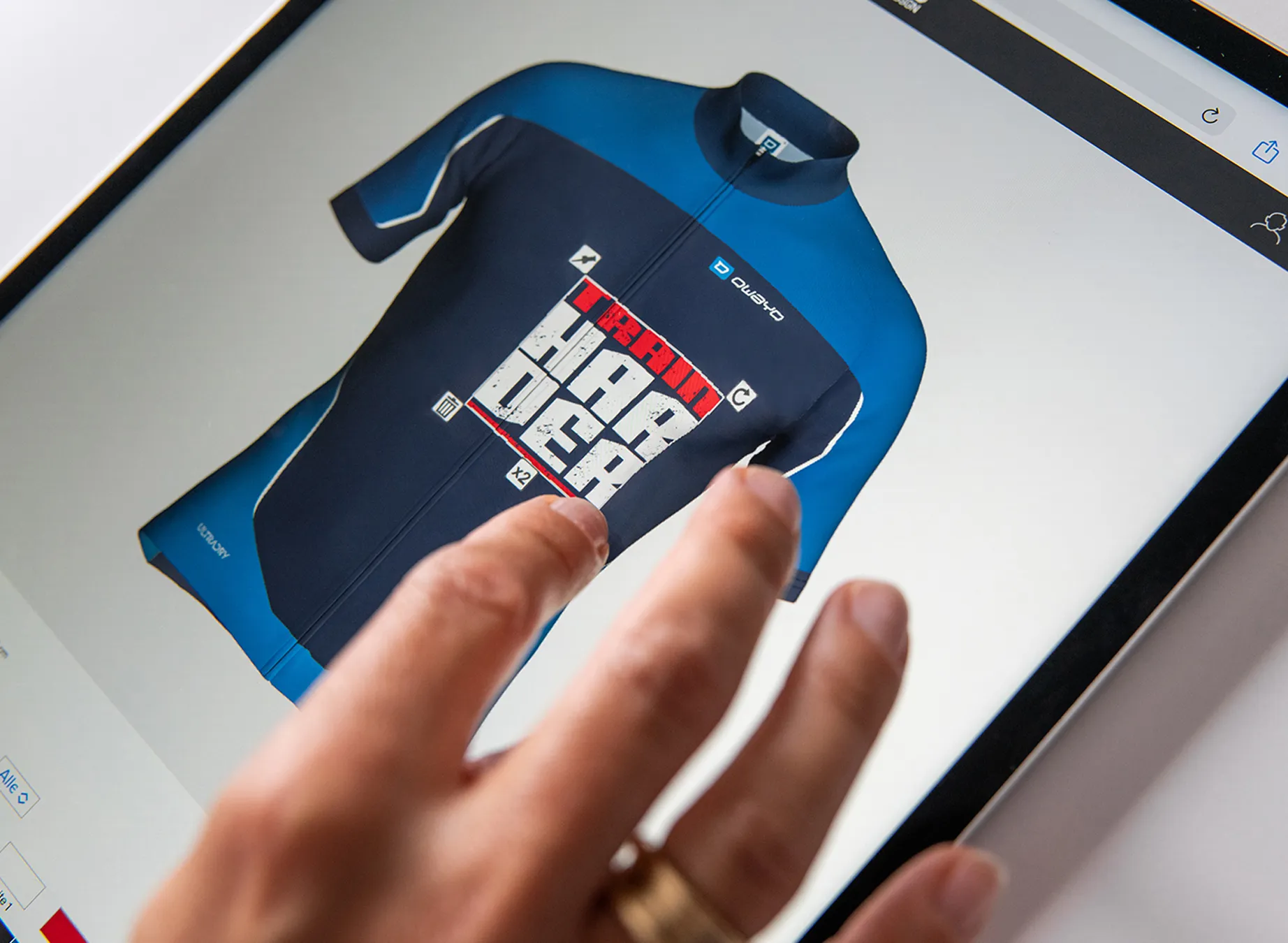 Eine Hand zeigt auf ein digitales Design eines blauen Sporttrikots mit dem Aufdruck 'train harder'.