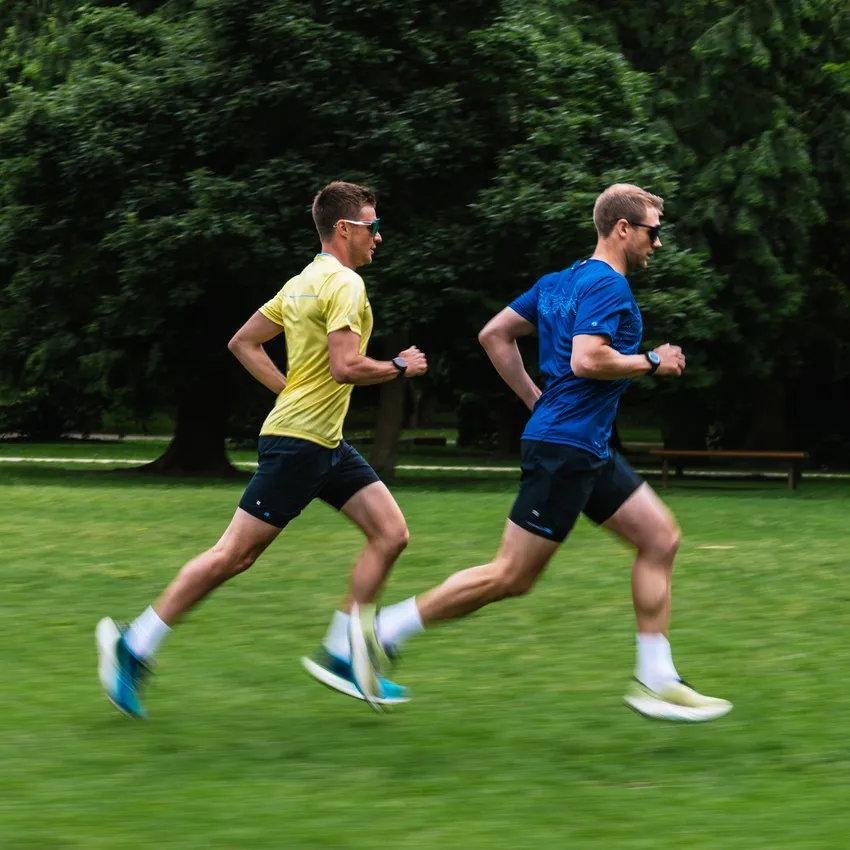 Zwei Männer in Sportbekleidung laufen auf einer Wiese.