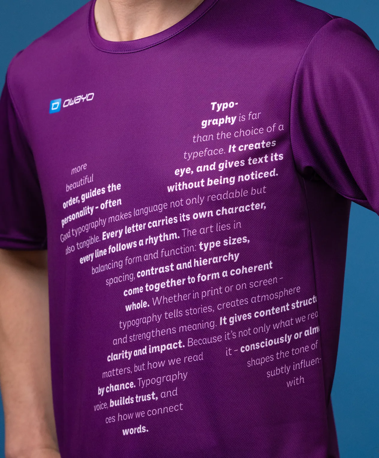 Ein naher Blick auf ein lila Sportshirt mit verschiedenen typografischen Texten auf der Vorderseite, das von einem Modell getragen wird.