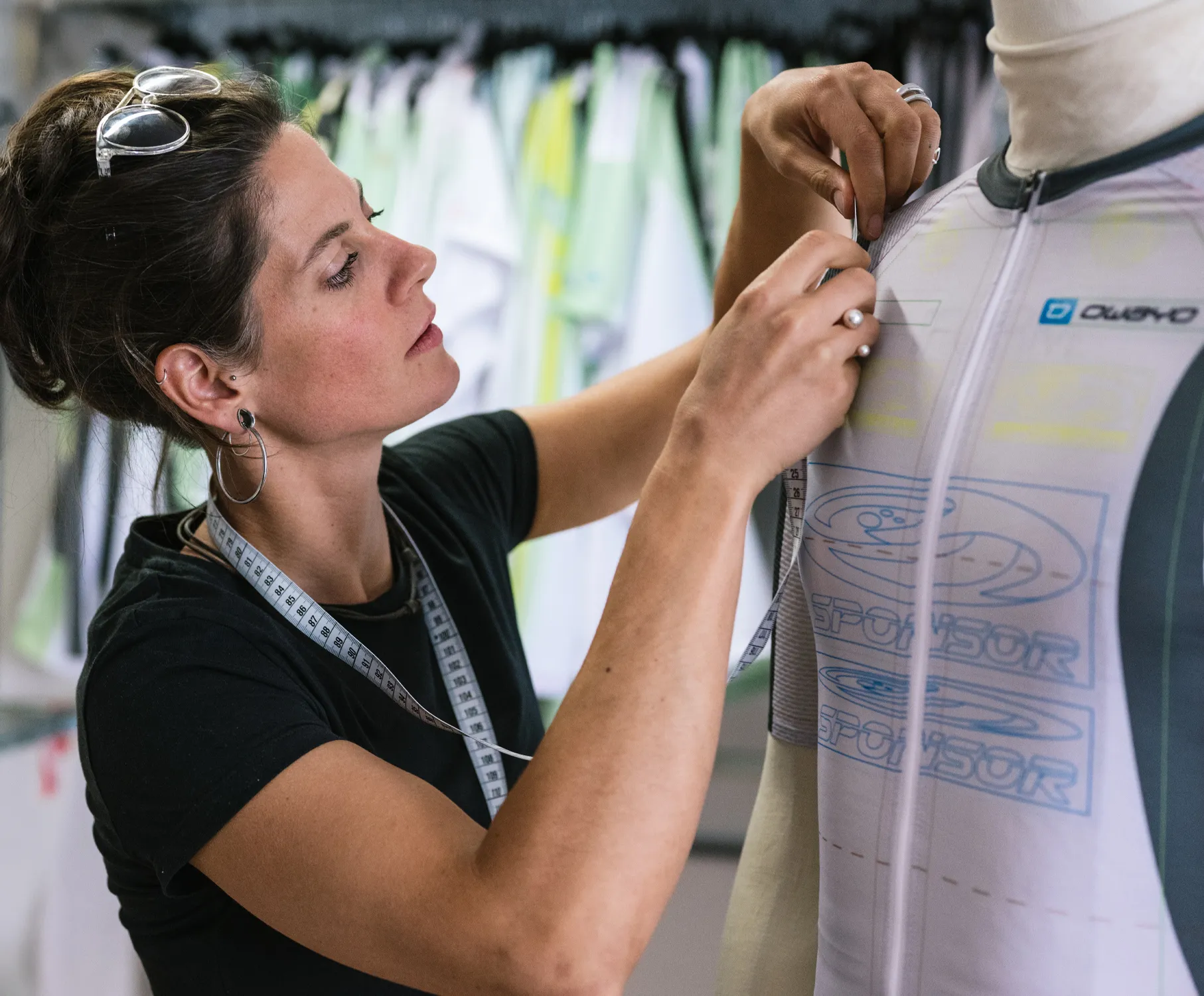 Eine Frau passt an einem Mannequin ein maßgeschneidertes Sporttrikot von owayo an, während sie ein Maßband um den Hals trägt.