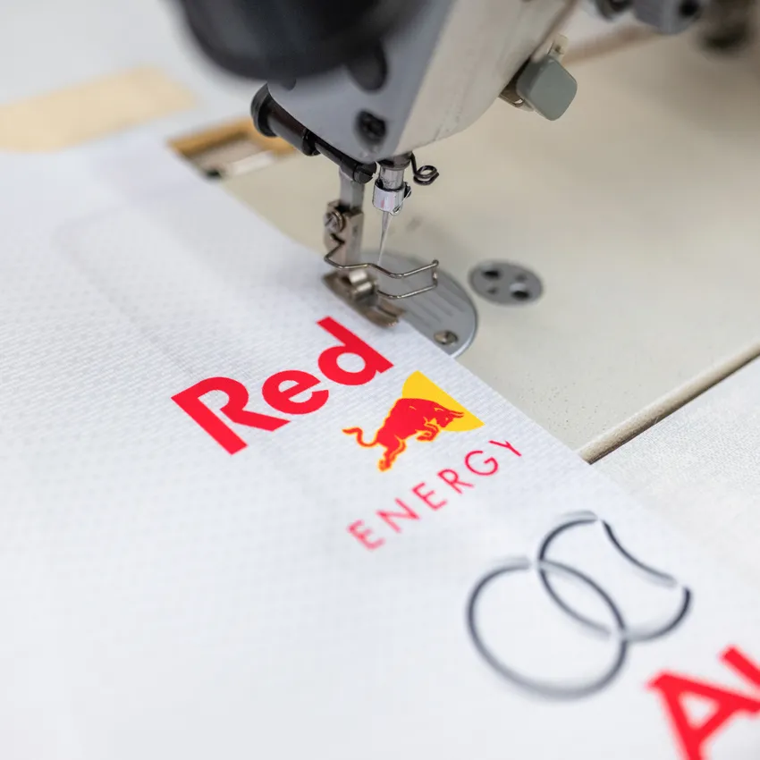 Eine Nähmaschine, die an einem weißen Stoff mit bunten Logos arbeitet.