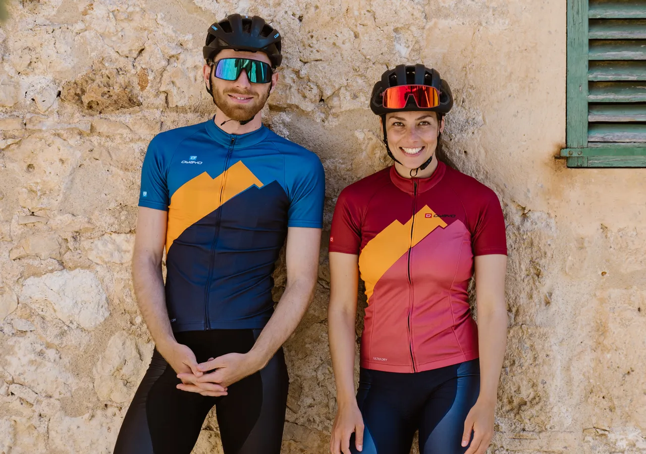 Ein Mann und eine Frau in maßgeschneiderten Sportbekleidungssets von owayo, die vor einer Steinmauer stehen.