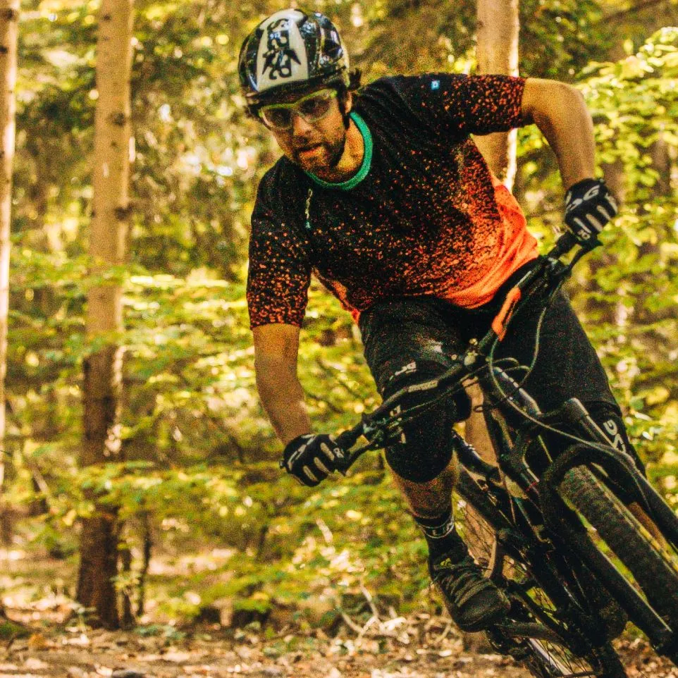 Ein Mountainbiker in einem schwarzen, rot-gepunkteten Trikot und schwarzen Shorts fährt durch einen Wald.
