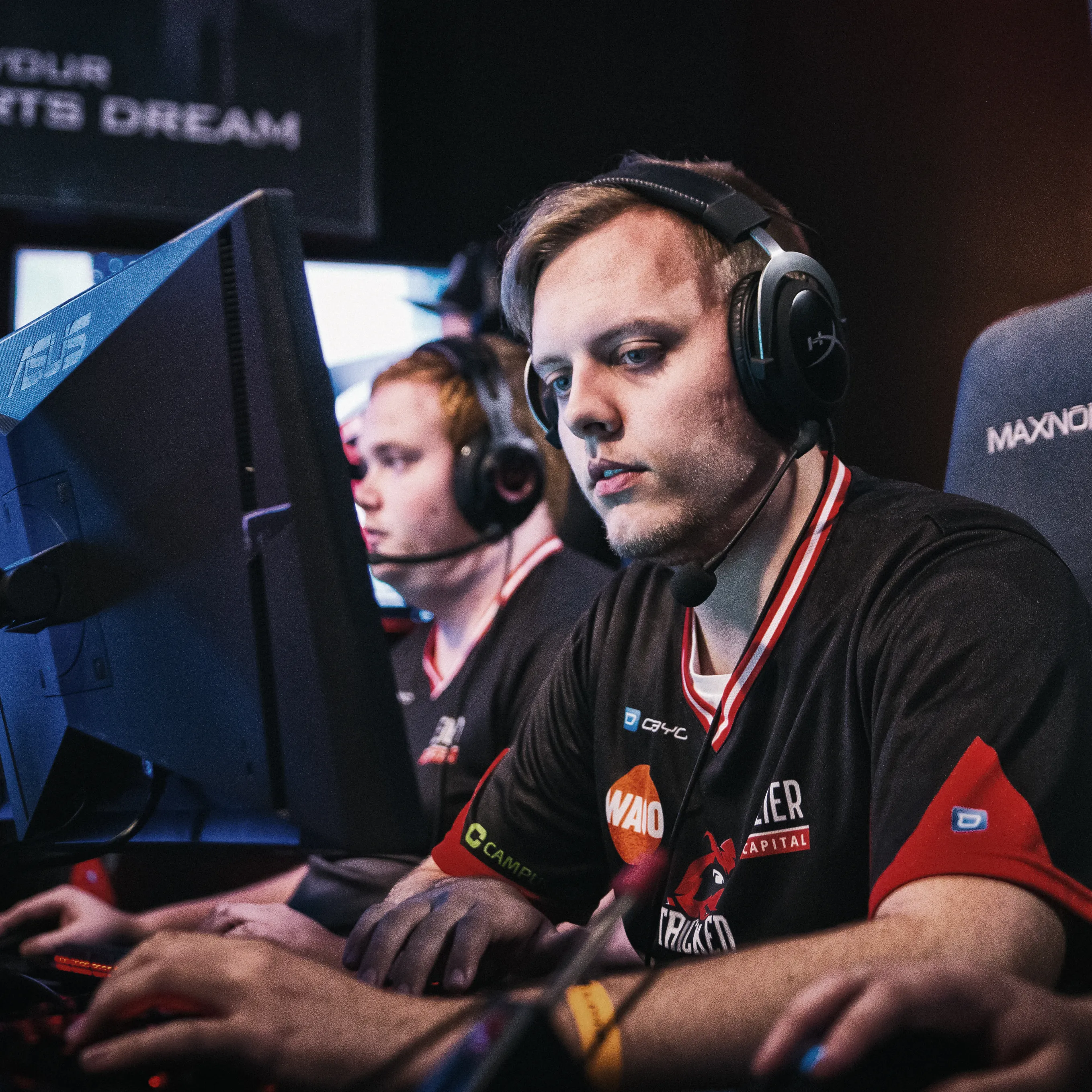 Zwei Spieler in sportlichen T-Shirts mit Headsets, die konzentriert an ihren Computern während eines eSports-Turniers spielen.